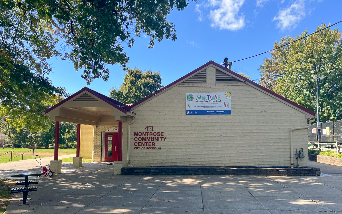 Exterior of the Montrose Community Center in Rockville, featuring a beige building with red trim, a banner, and nearby trees under a blue sky.