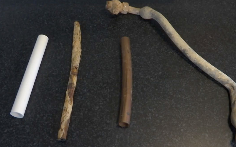 Four different types of pipes, including a white plastic pipe, a rusted metal pipe, a copper pipe, and an old corroded pipe, are laid out on a dark surface.