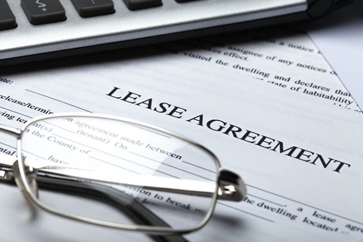 A pair of eyeglasses and part of a calculator rest on a lease agreement document.