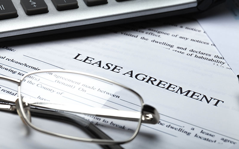 A pair of eyeglasses and part of a calculator rest on a lease agreement document.