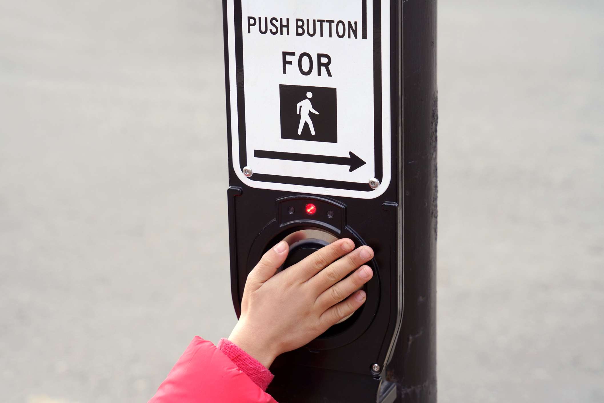 A person presses a pedestrian crossing button at a crosswalk, indicated by a sign above the button.