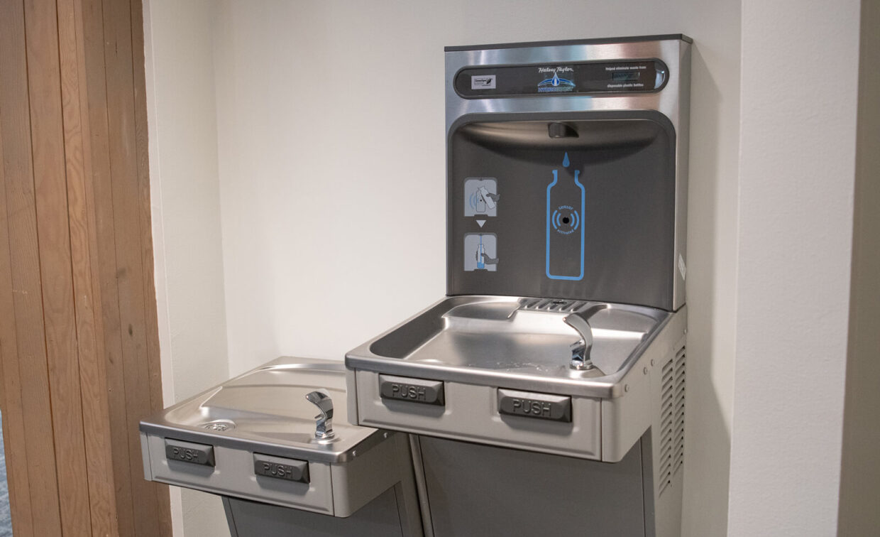 Two stainless steel water fountains are mounted on a wall, one with a standard spout and the other with a bottle filling station above the bubbler.