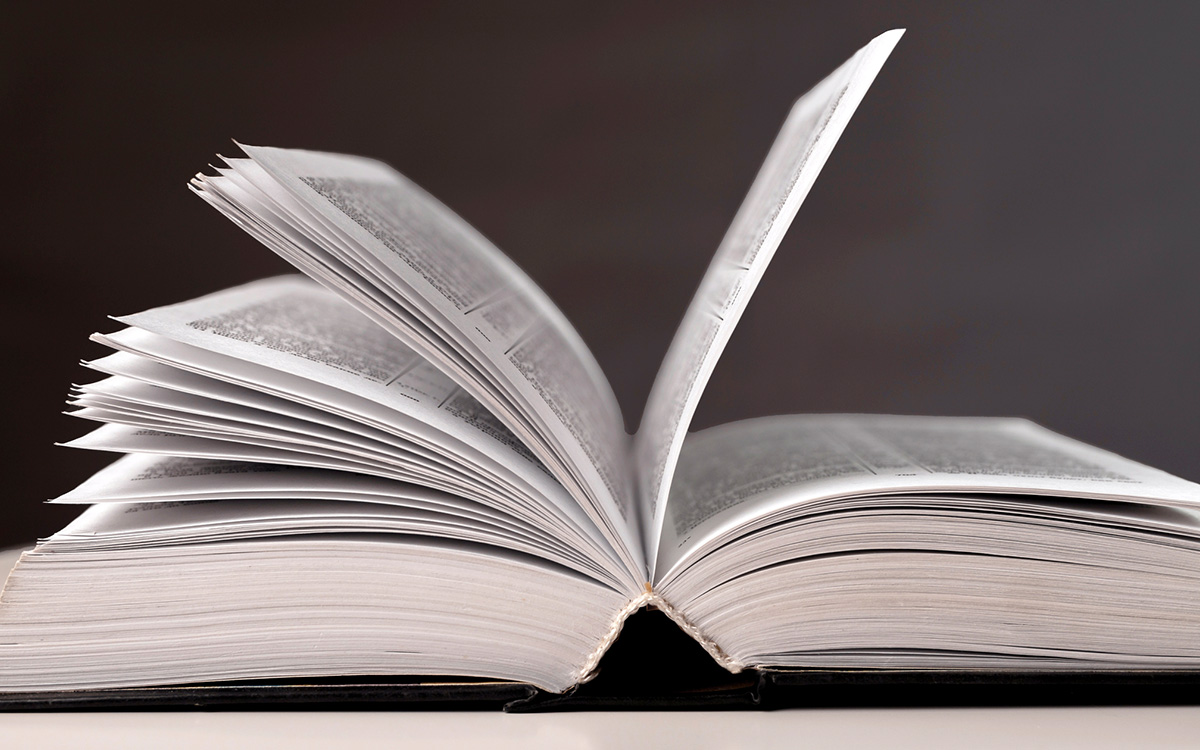 An open book viewed from the side with several pages flipping upward against a plain dark background. An open book viewed from the side with several pages flipping upward against a plain dark background.