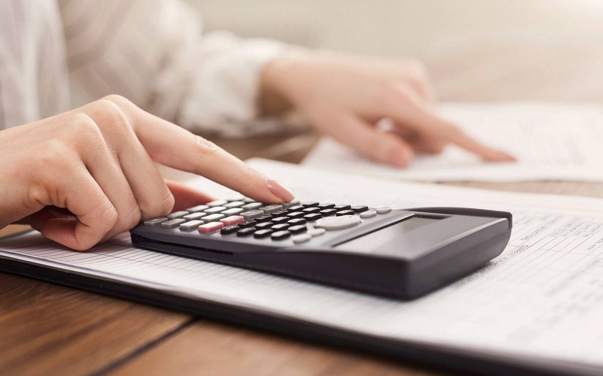 A person uses a calculator while reviewing financial documents on a desk. A person uses a calculator while reviewing financial documents on a desk.