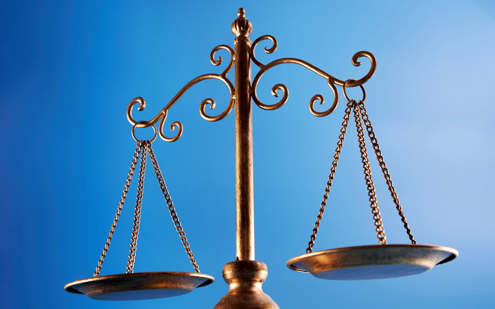 A close-up of a bronze balance scale with two empty pans against a blue background.
