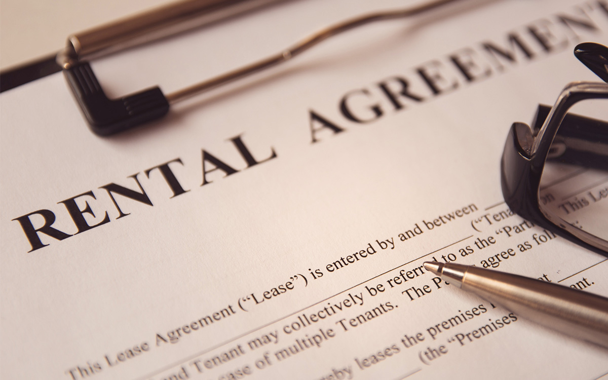 Close-up of a rental agreement document with a pen, glasses, and part of a clipboard visible.