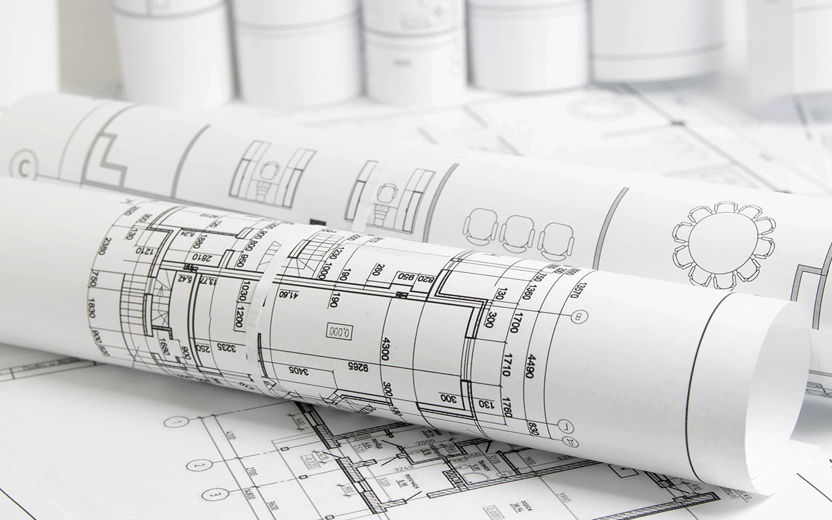 Two rolled architectural blueprints rest on top of additional floor plans, displaying detailed technical drawings and measurements. Two rolled architectural blueprints rest on top of additional floor plans, displaying detailed technical drawings and measurements.