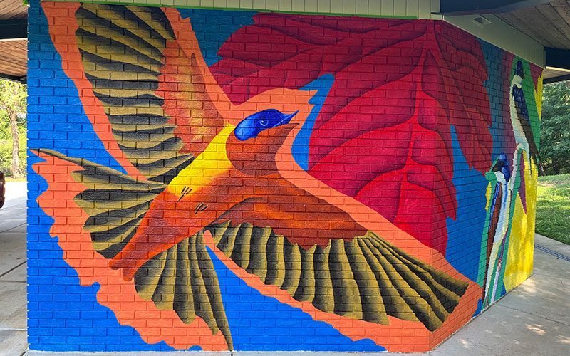 A mural painted on a brick wall shows a large bird with yellow and brown wings in flight against a background of red leaves and blue sky.