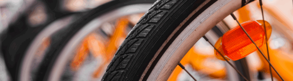 Image depicts a close up of a bicycle wheel in the foreground, with other bikes in the background.