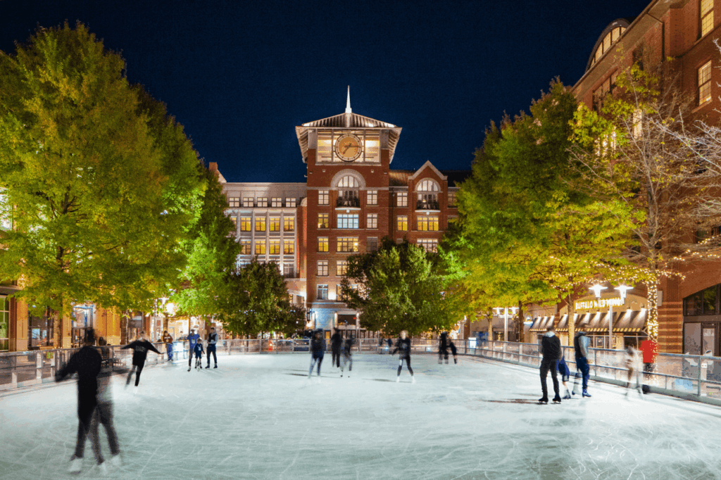 Rockville Town Square ice skating rink with ice skaters and the clocktower in the background.