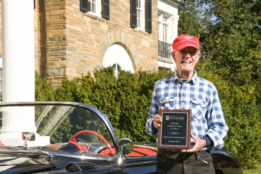 Cal Milans standing with his 1957 Chevrolet Corvette in front of the Glenview Mansion with his Mayor and Council Award