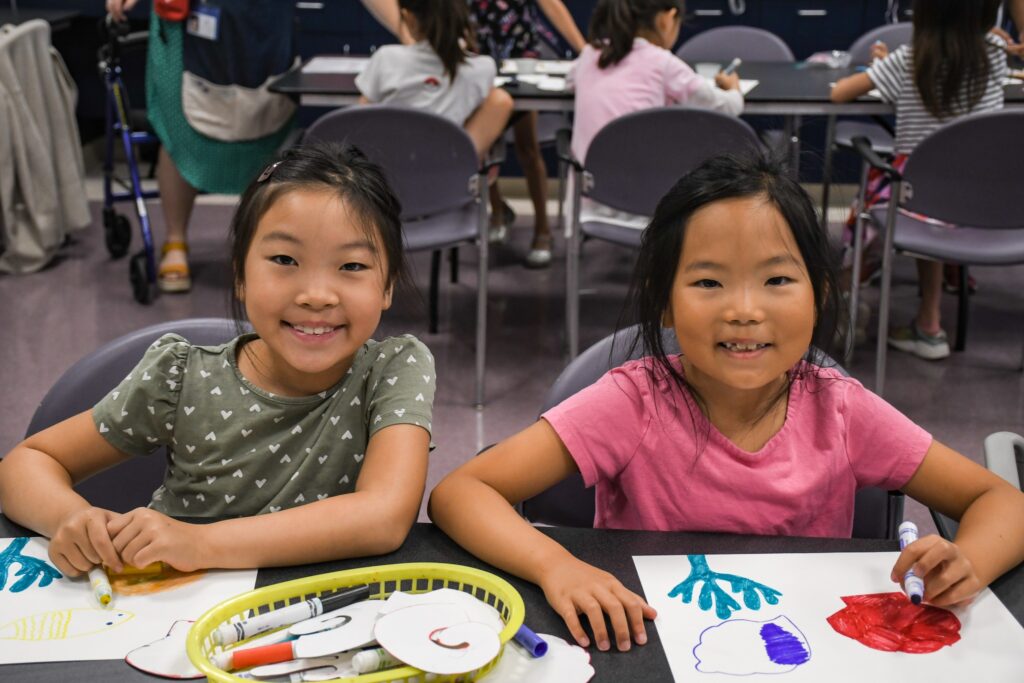 Two girls smile as they work on art projects