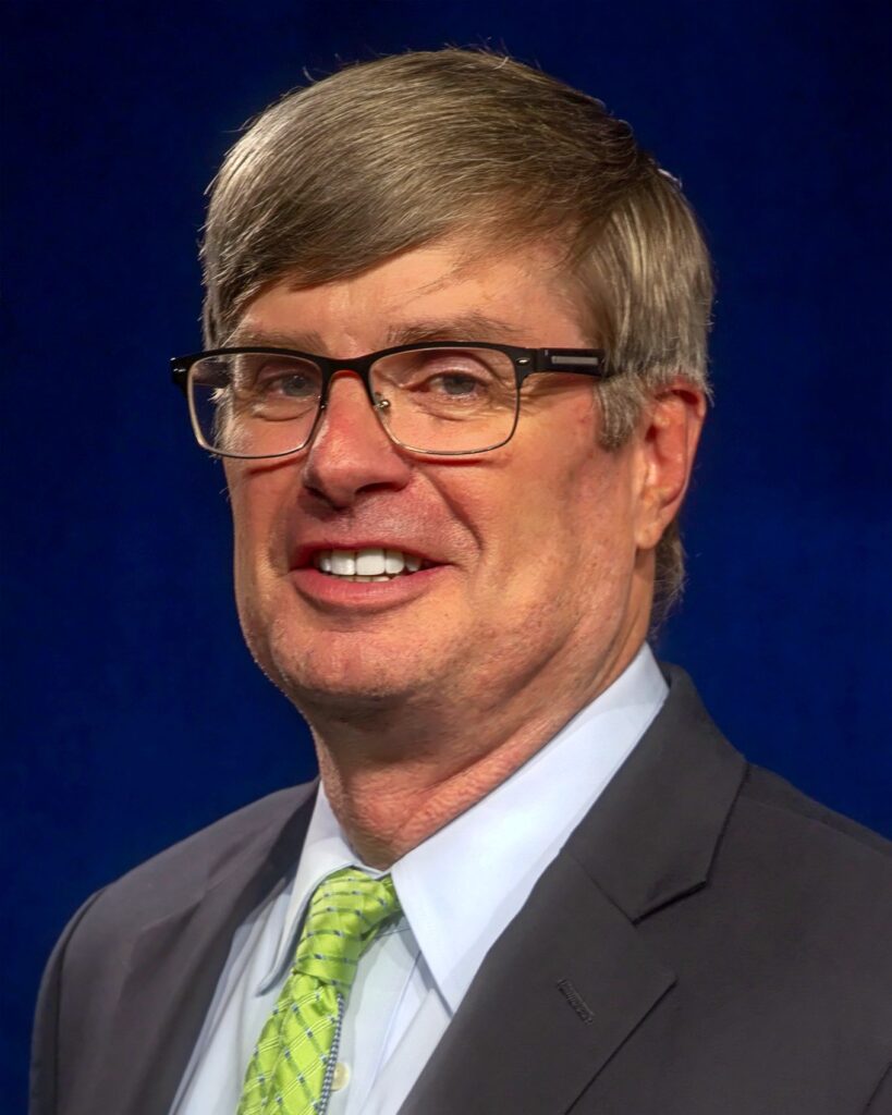 Headshot photo of Craig L. Simoneau, acting city manager, in dark suit coat, green tie and black wire-frame glasses.