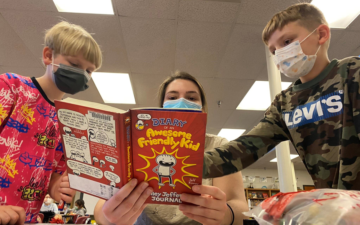 Three children wearing masks read the book 