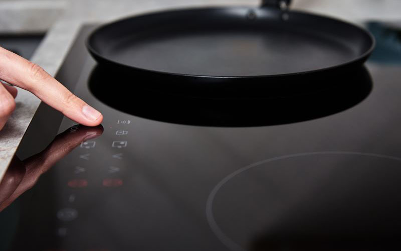 A person presses a button on a touch control panel of an induction cooktop with a frying pan placed on top.