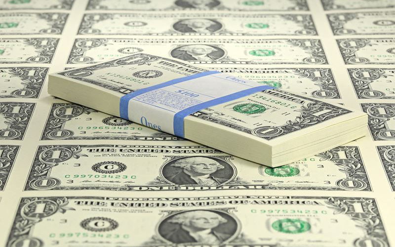 A stack of bundled one-dollar bills placed on top of a spread of loose one-dollar bills.