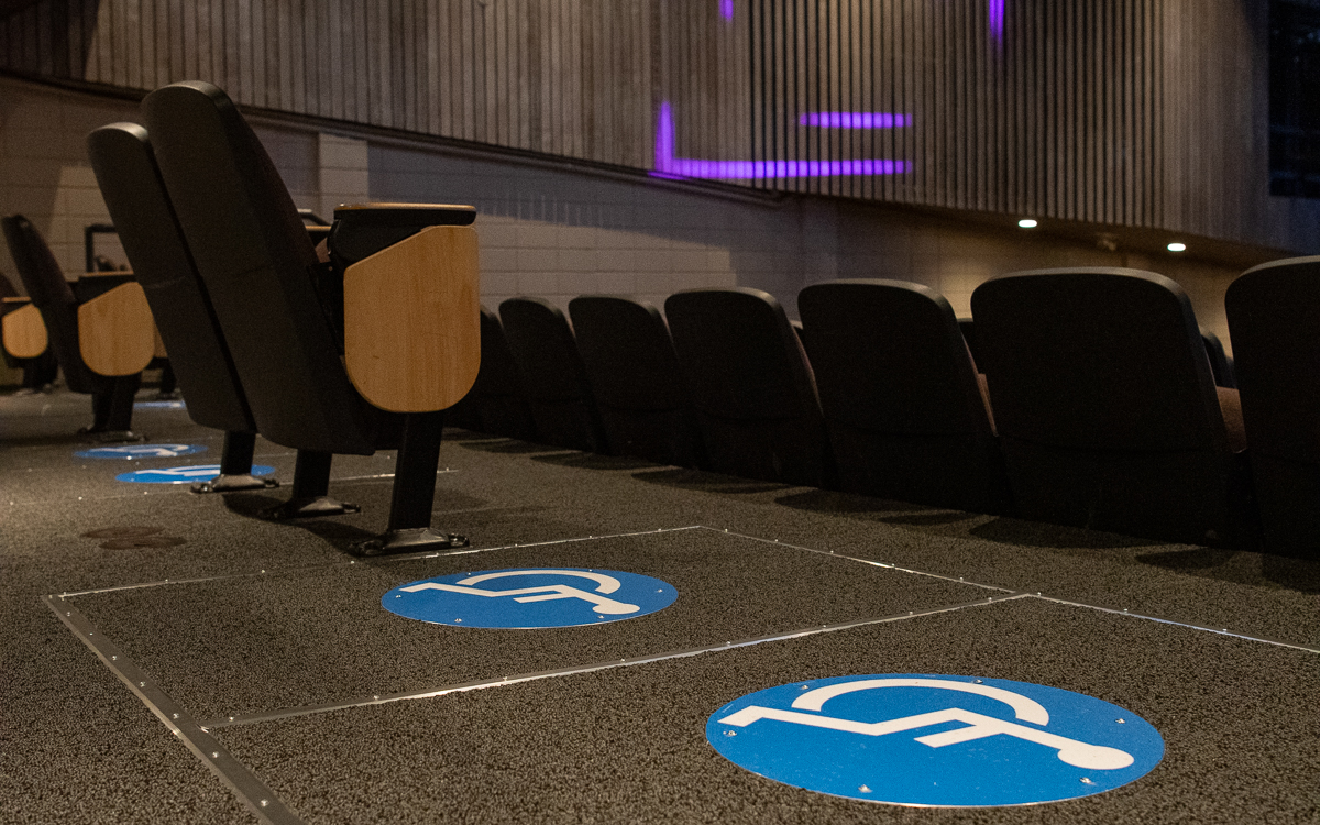 Rows of theater seats with blue wheelchair accessibility symbols marked on the floor in front of them.