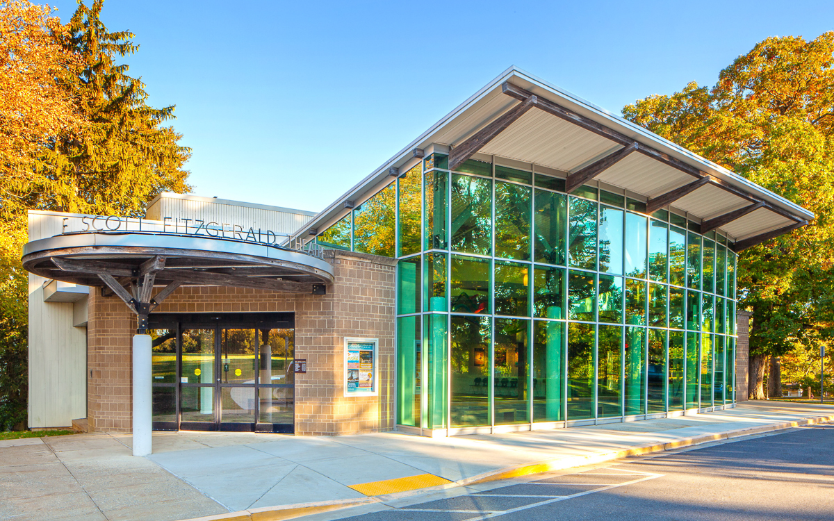 Modern building with large glass windows and an overhang at the entrance, surrounded by trees and bathed in sunlight. The sign reads "SCOTT FITZGERALD" above the door.
