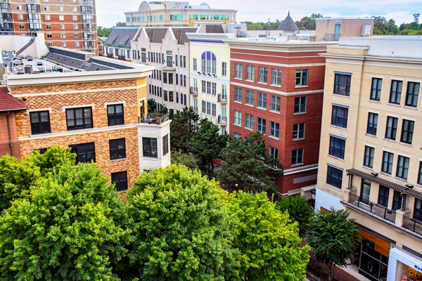 View of several mid-rise apartment buildings with varied facades surrounded by leafy green trees in an urban area.
