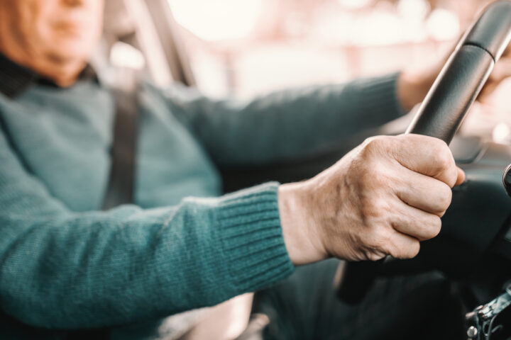 Close-up of a person wearing a green sweater and seatbelt, holding a steering wheel while driving a car.