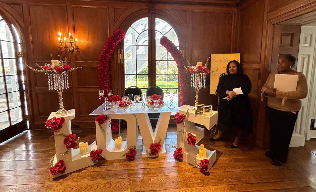 A table decorated with red roses and candles sits atop large letters spelling 