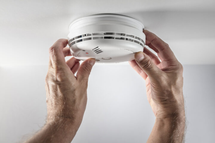 Two hands are installing or testing a smoke detector on a white ceiling.