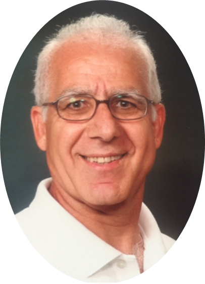 An older man with short white hair, glasses, and a white collared shirt smiles at the camera against a dark background.