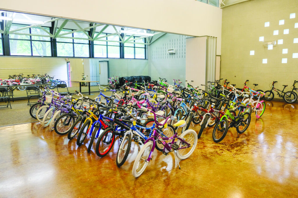 Dozens of colorful bicycles are arranged in rows on a shiny indoor floor, with more bikes visible against the walls in the background.