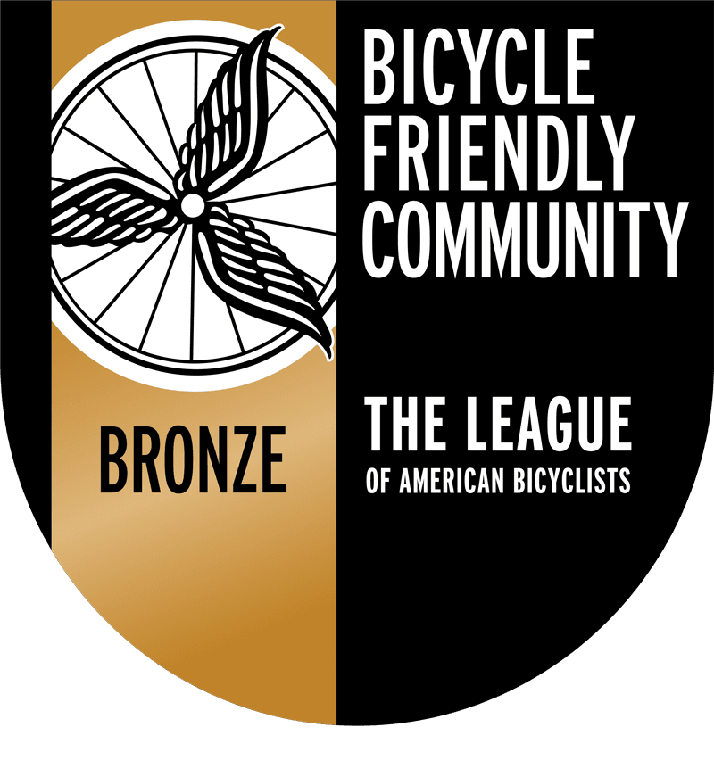 A badge with a bicycle wheel graphic, labeled "Bicycle Friendly Community Bronze" and "The League of American Bicyclists.