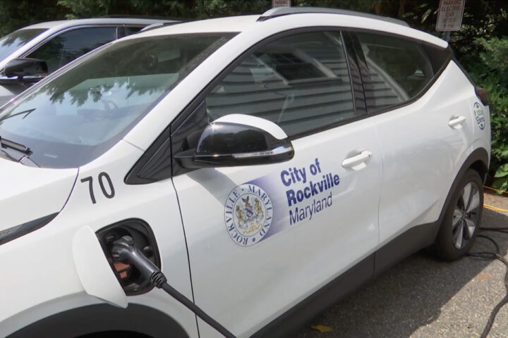 A white City of Rockville, Maryland electric vehicle is parked and charging at an outdoor charging station.