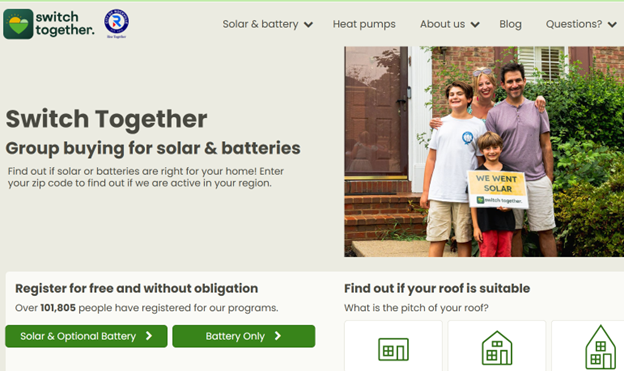 A family of four smiles outside their home, holding a 