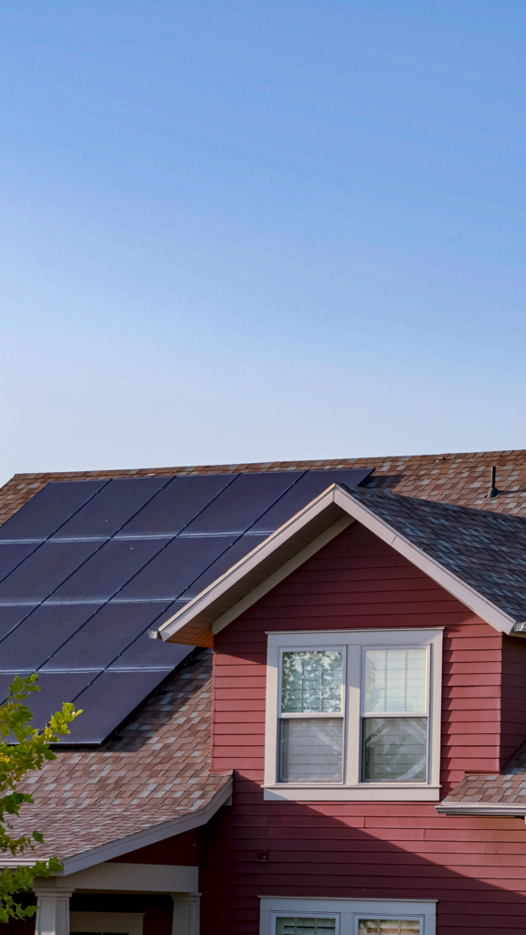 A red house with solar panels installed on its roof under a clear blue sky.