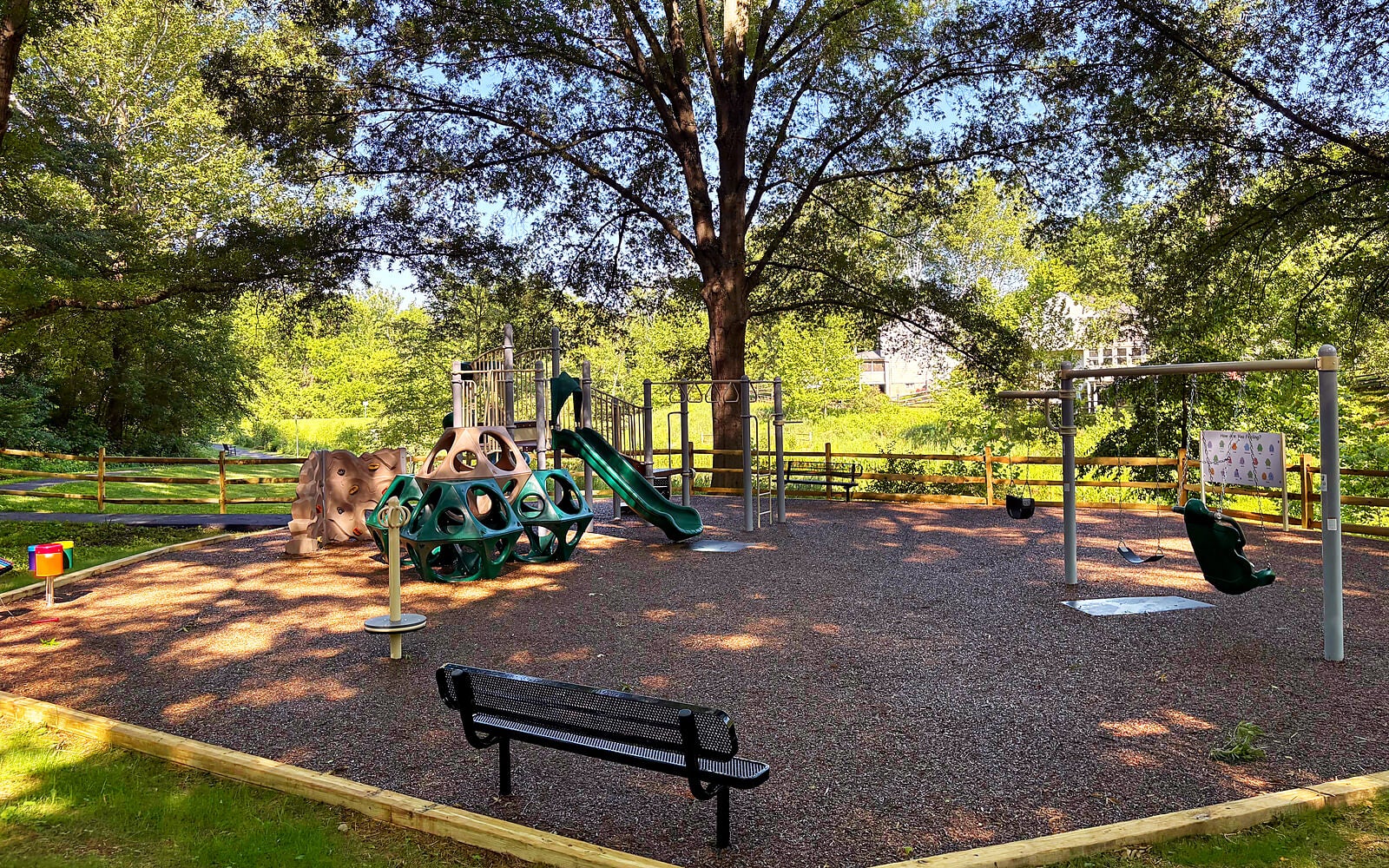 A playground with slides, swings, and a climbing wall surrounded by trees.