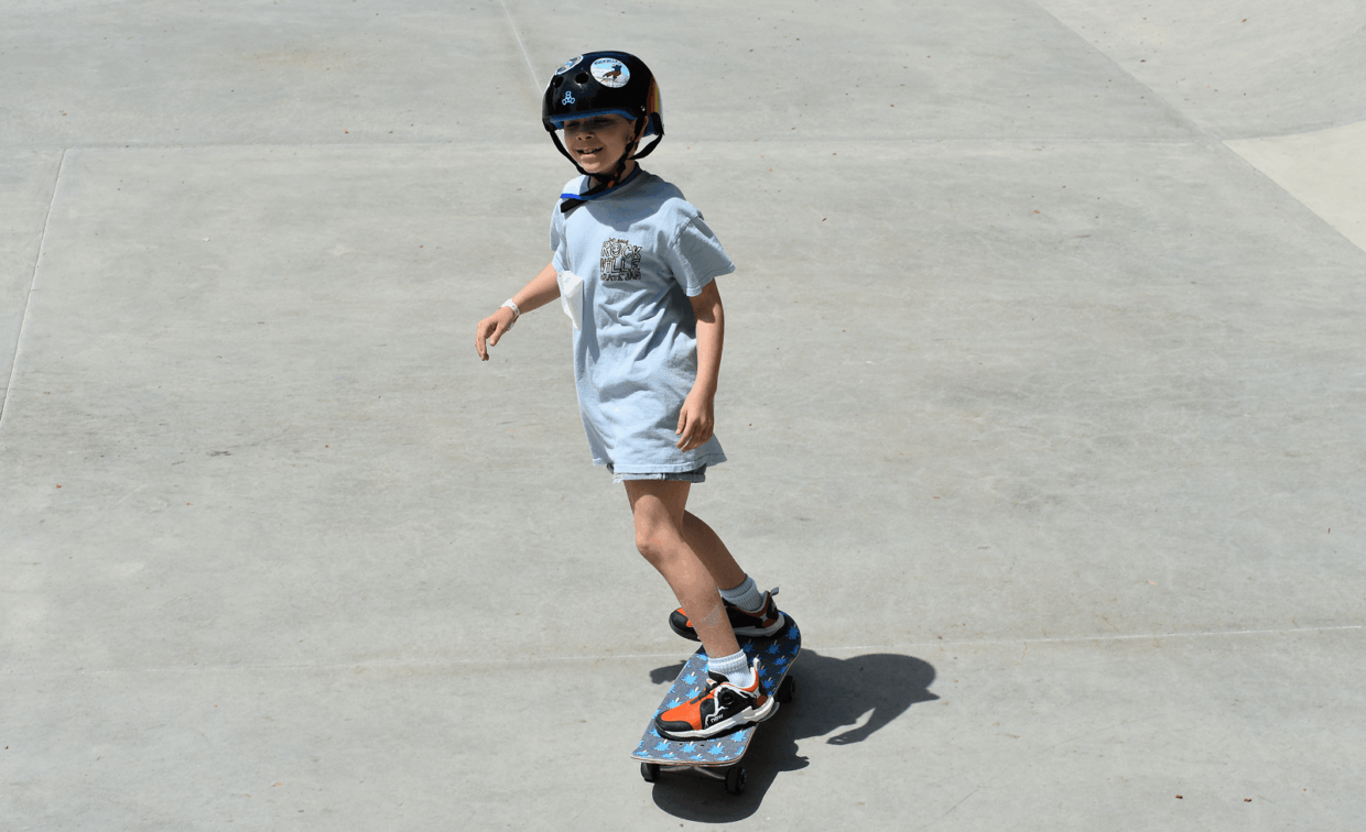 A child wearing a helmet skateboards on a smooth concrete surface in bright sunlight.