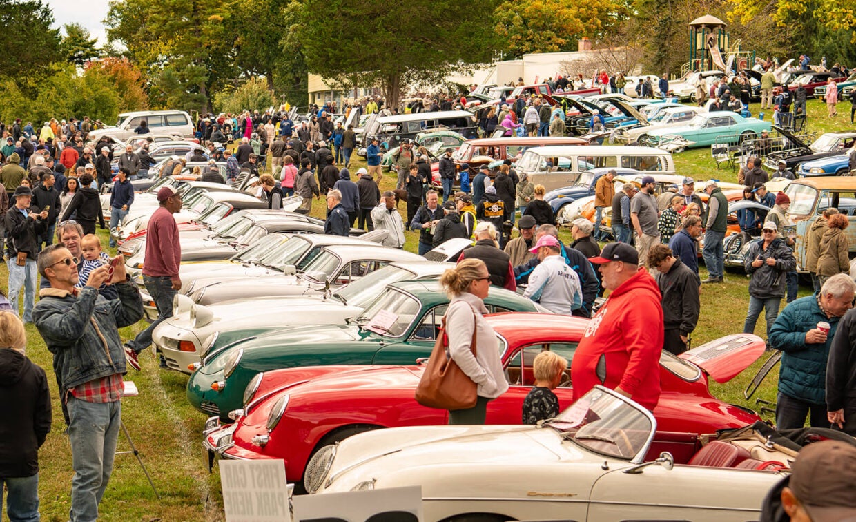 A large outdoor car show featuring many rows of vintage Porsche sports cars parked on a grass field with crowds of spectators.