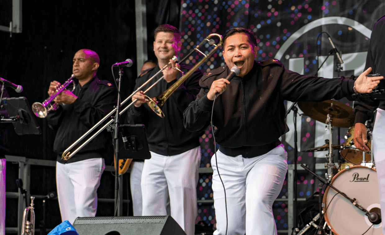 A vocalist and two brass musicians in matching black jackets and white trousers performing on stage.