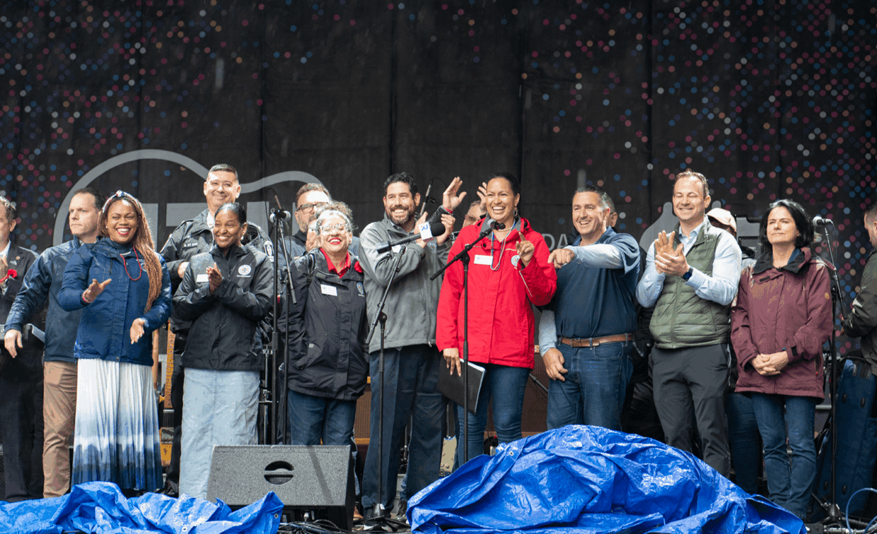 A group of people standing on a stage, some speaking into microphones and others clapping.