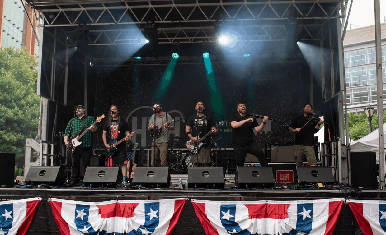 A folk-punk band performing on an outdoor stage decorated with red, white, and blue bunting.