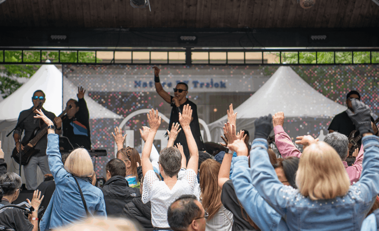 A performer sings on stage in front of an audience with their arms raised.