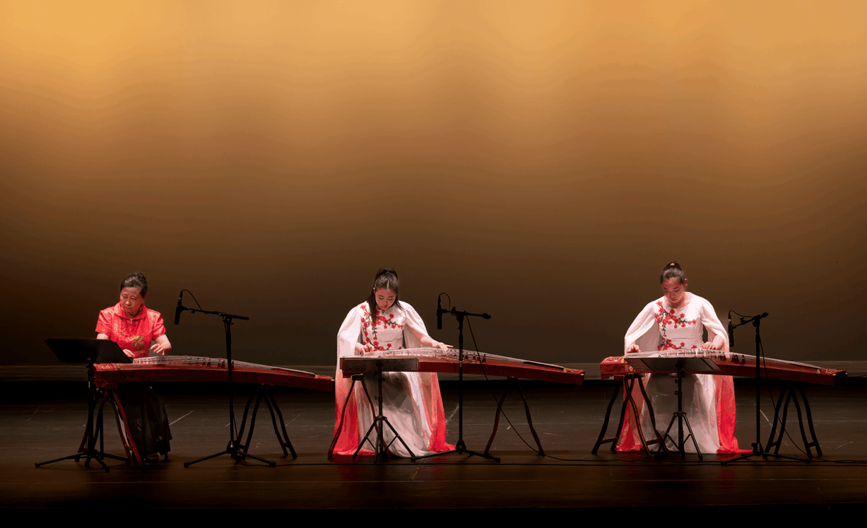 Three musicians performing on guzheng instruments on a stage.