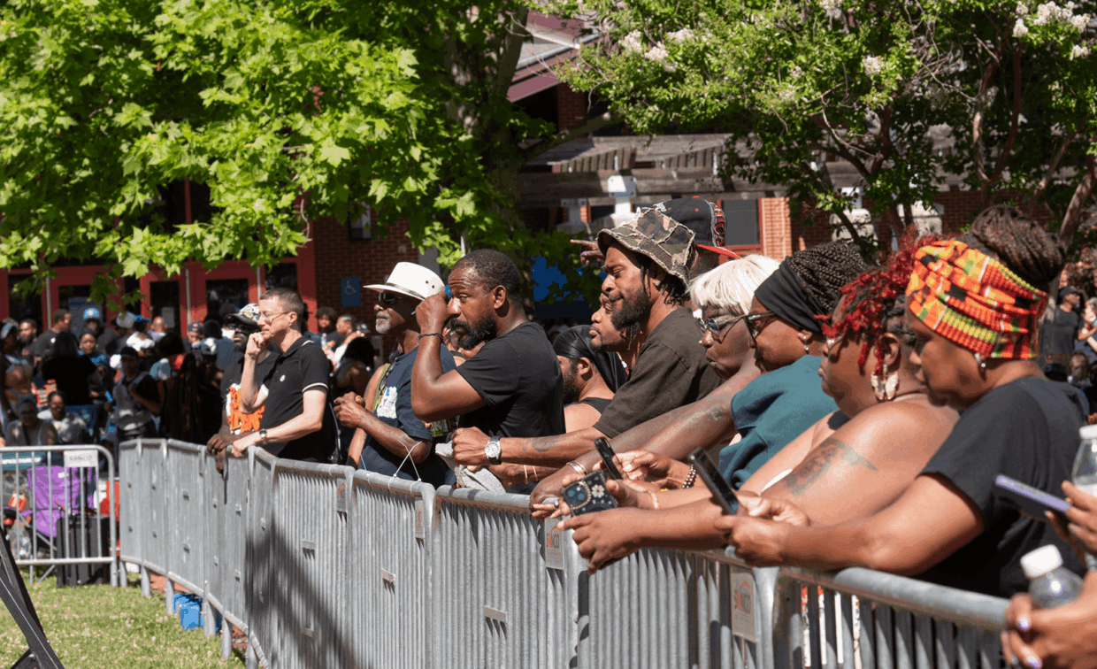 A crowd of people standing behind a metal barricade at an outdoor event.