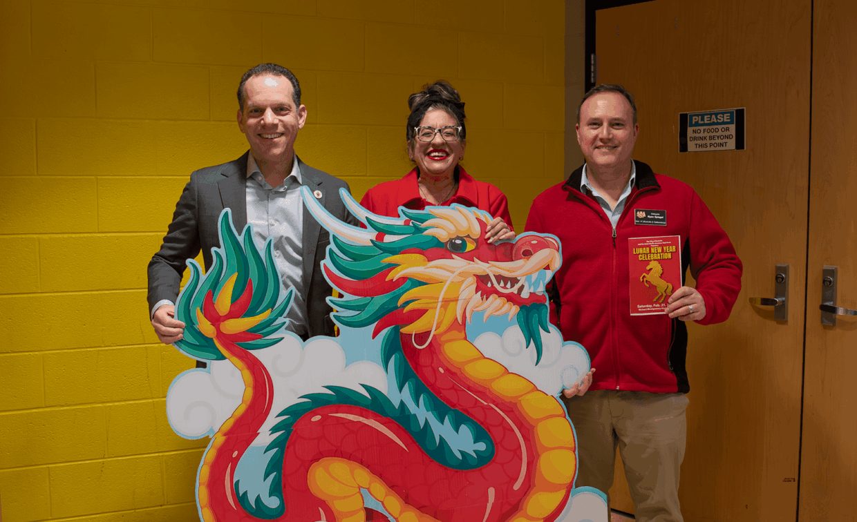 Three people holding a large cutout of a colorful Chinese dragon, with the person on the right holding a flyer for a Lunar New Year celebration.