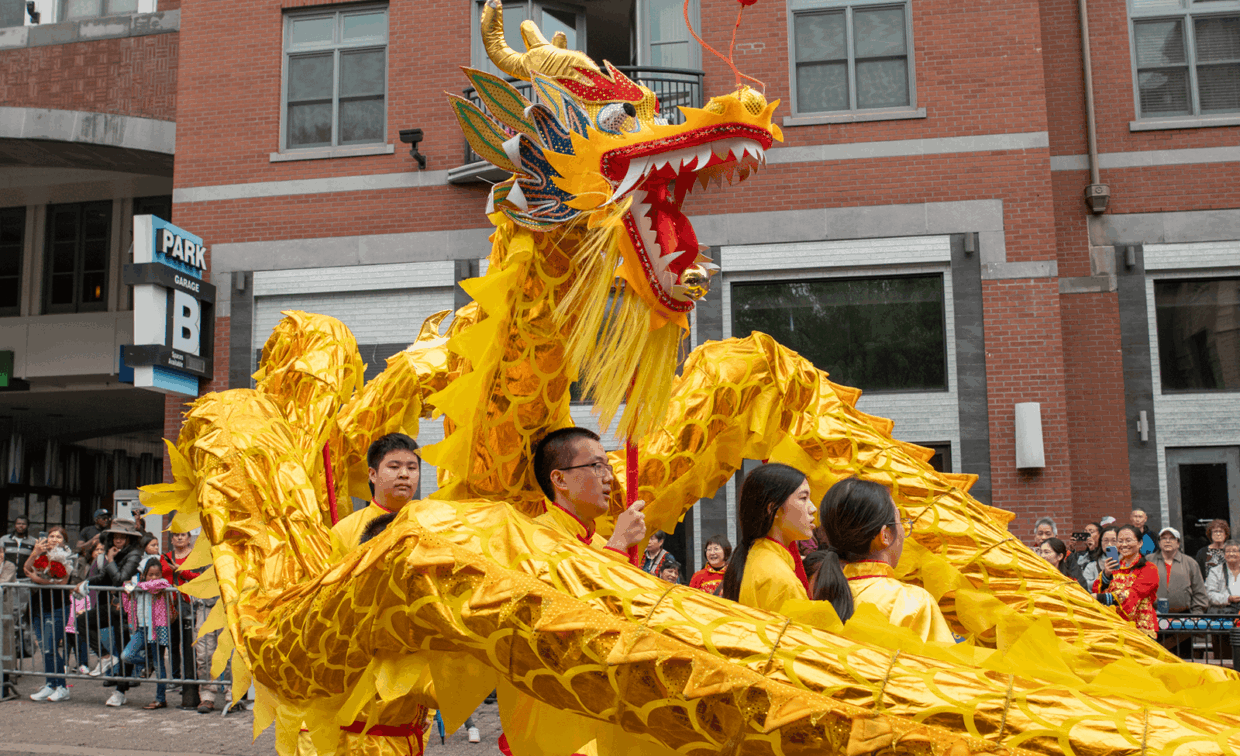 Performers carry a large, yellow Chinese dragon puppet through a city street.