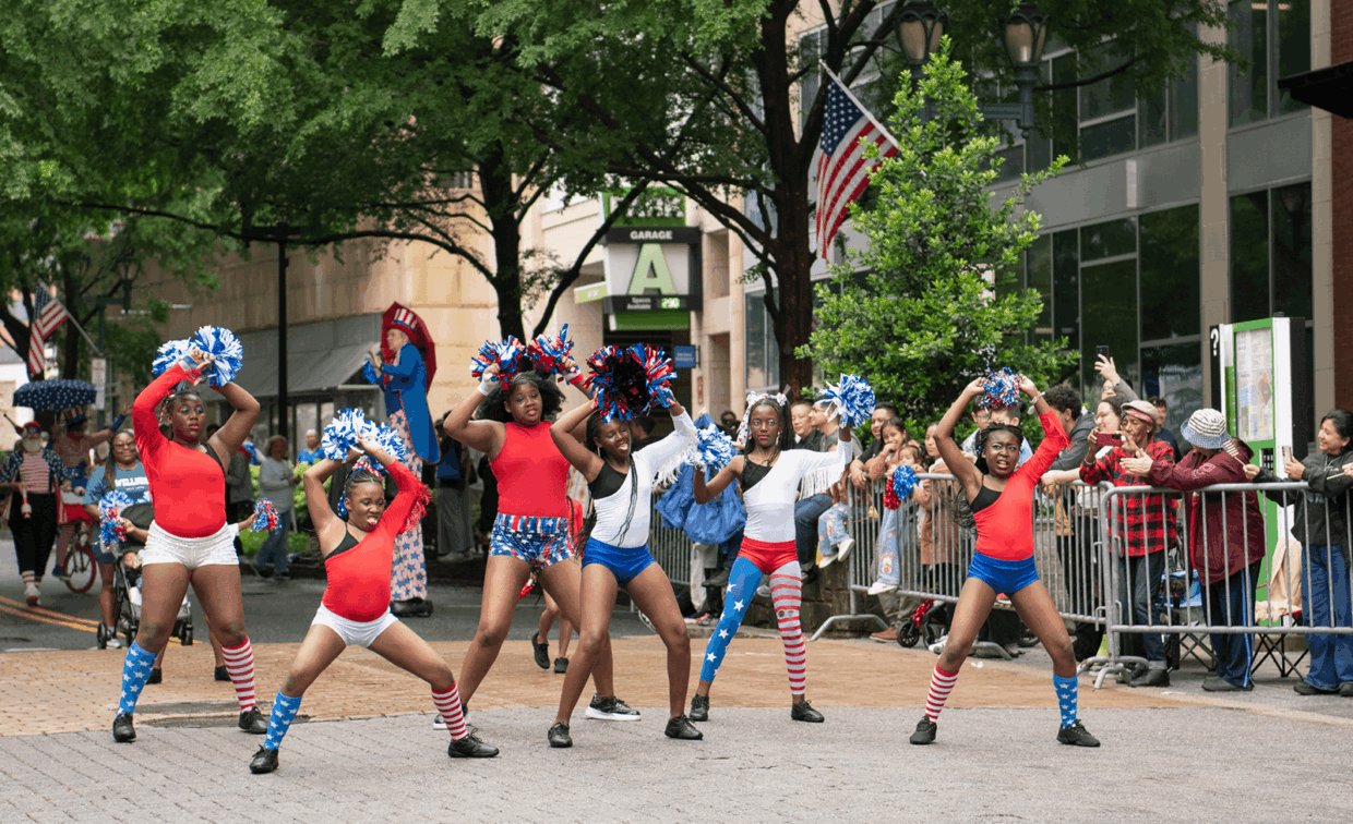 Six cheerleaders in red, white, and blue uniforms perform in front of a crowd at a parade.