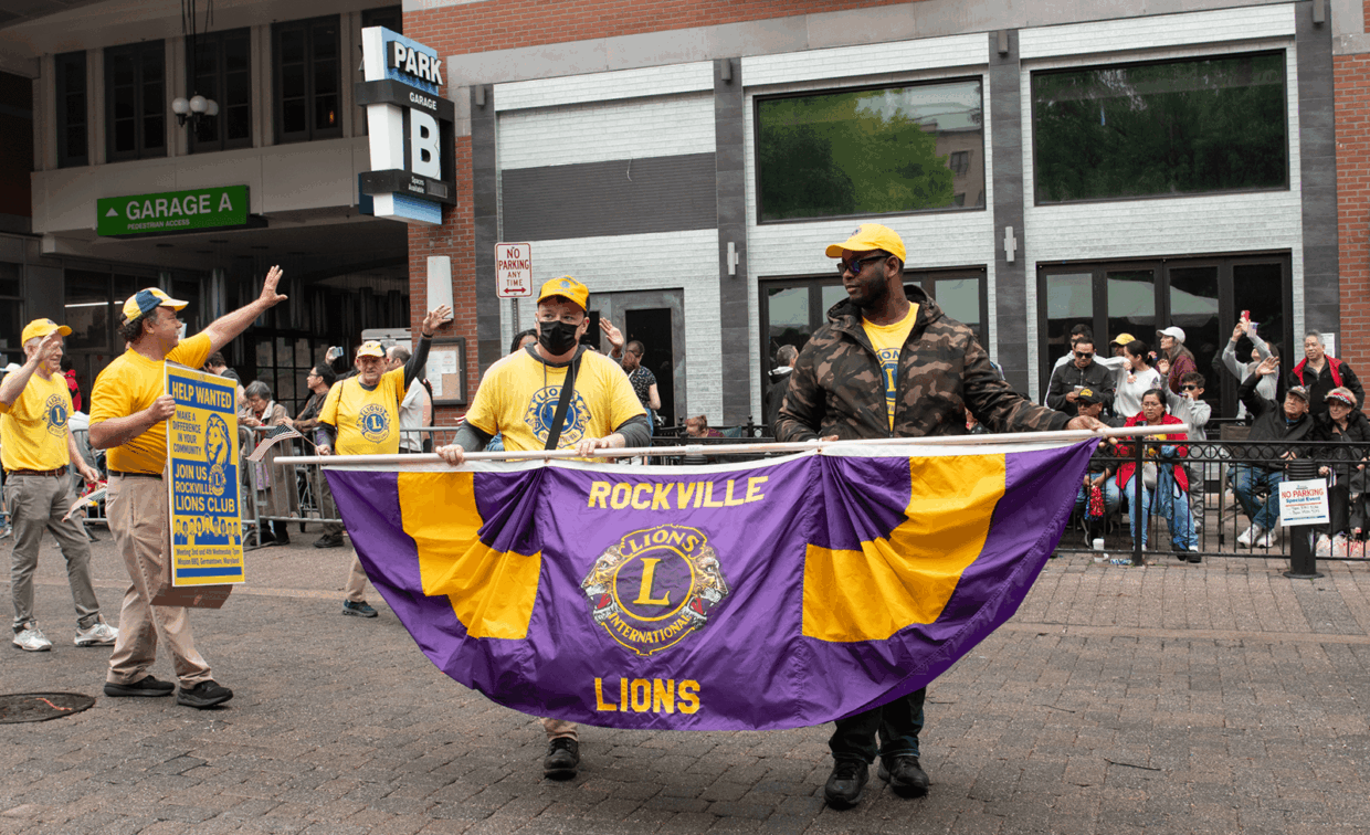 Members of the Rockville Lions Club carrying a purple and yellow club banner during a street parade.