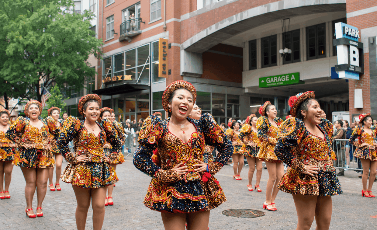 A group of dancers in ornate, colorful, beaded costumes perform in a city street.