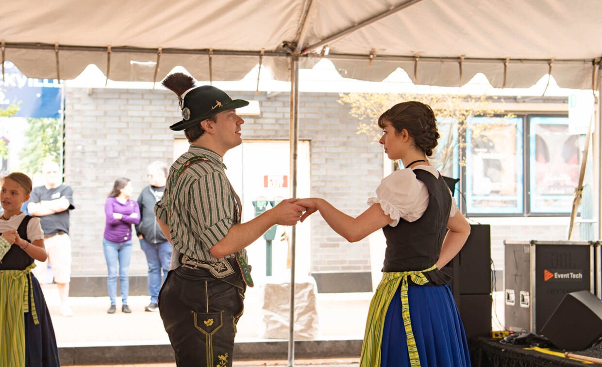 A man and woman in traditional Bavarian clothing hold hands while dancing under a tent.