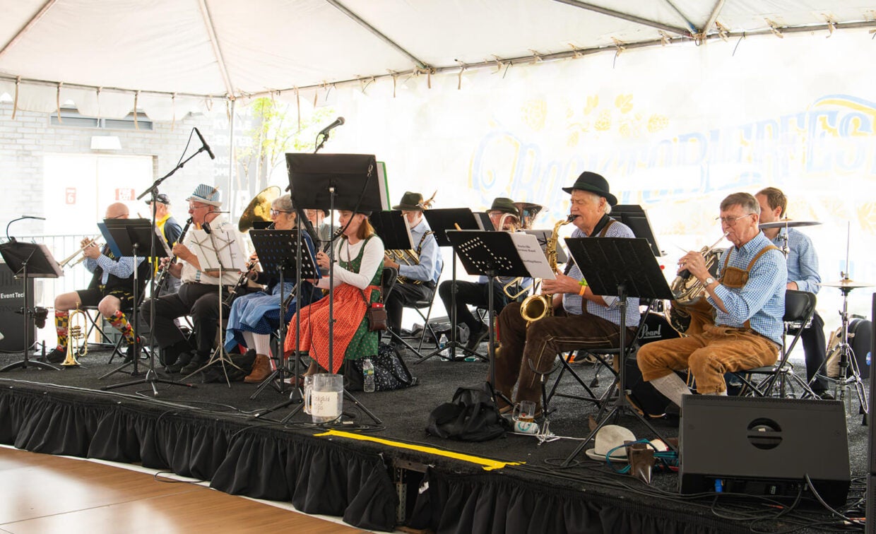 A brass band plays instruments on a stage under a white tent.