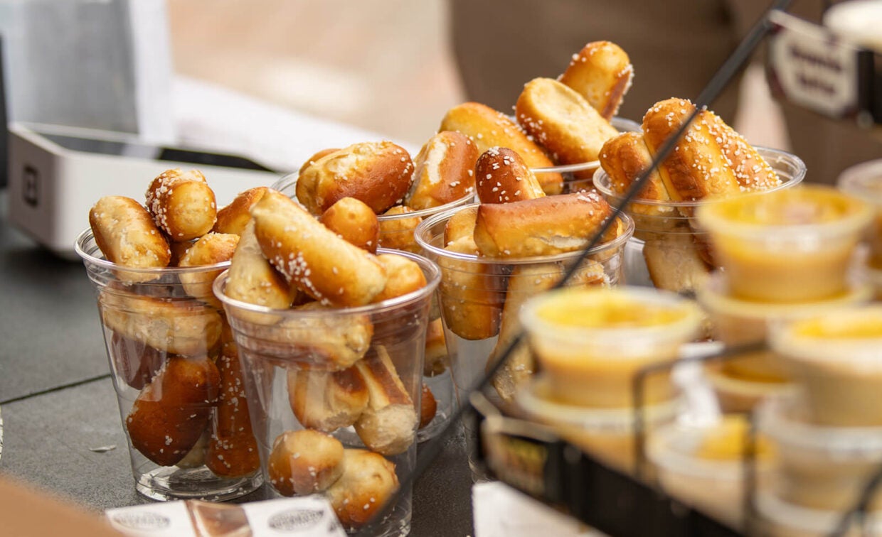 Clear plastic cups filled with salted pretzel bites, accompanied by small containers of dipping sauce.